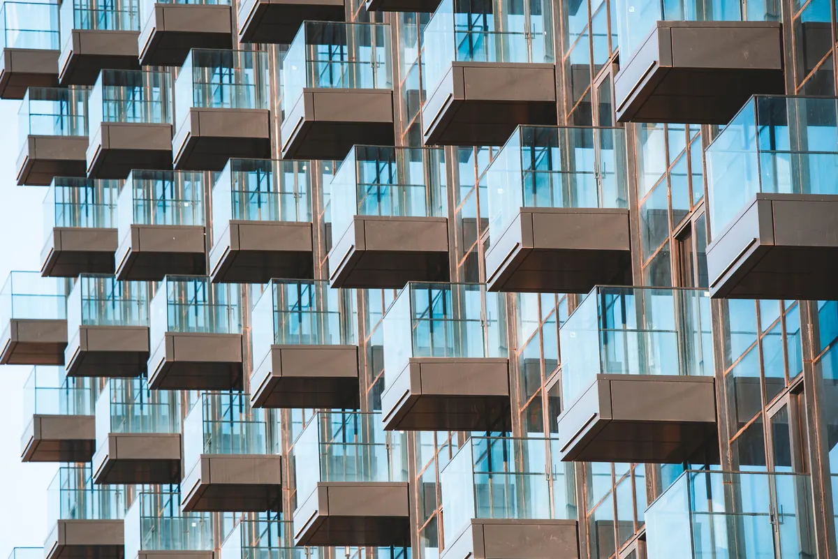 Tower facade of cantilevered balconies with glass railings stacked in a staggered pattern against a blue sky