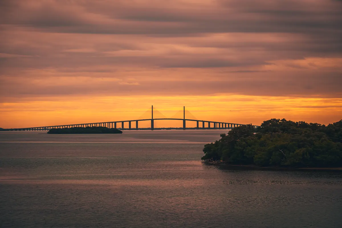 Sunshine Skyway Bridge silhouetted against an orange sunset, with a mangrove island and still water in front